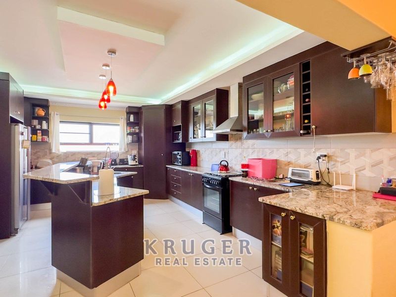 Spacious kitchen featuring dark wood cabinetry, granite countertops, integrated appliances, and modern recessed ceiling lighting with a breakfast nook area.
