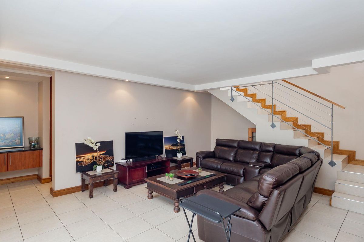 Spacious living room featuring tiled flooring, recessed lighting, and an open-plan staircase with timber treads and a modern metal balustrade.