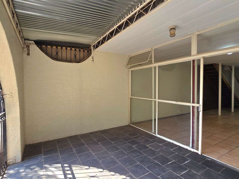A covered patio area featuring tiled flooring, a corrugated metal roof, and a large sliding glass door providing access to the interior living space.