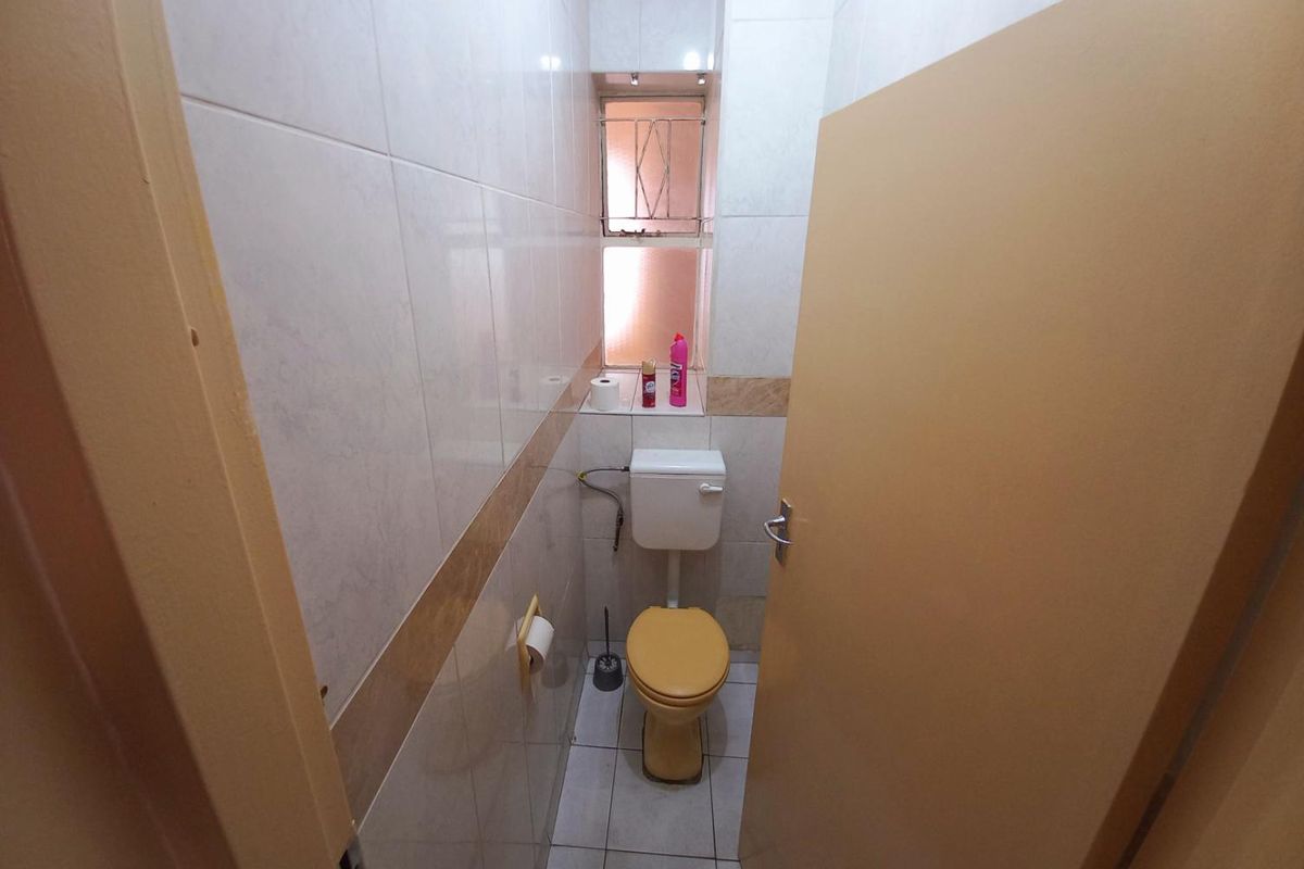 A compact guest bathroom featuring floor-to-ceiling wall tiles, a standard toilet, and a small window for natural ventilation.