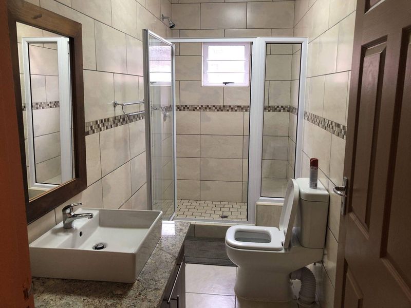 A well-maintained bathroom featuring a modern vessel sink on a granite vanity, a glass-enclosed shower, and neutral wall tiling.
