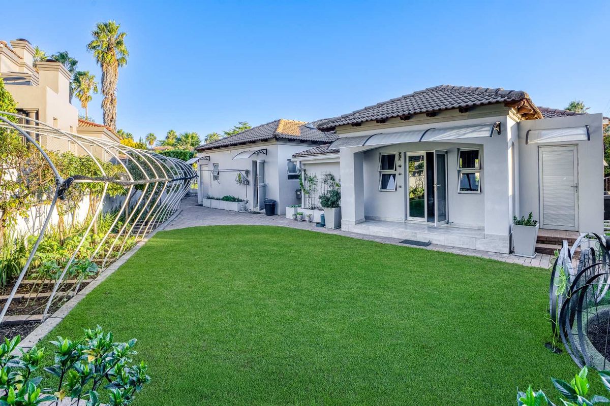 A well-maintained rear garden featuring a manicured lawn, paved pathways, and a covered patio area attached to the main dwelling.