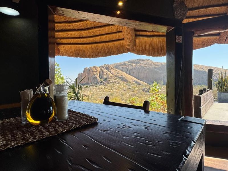 A covered outdoor patio area featuring a traditional thatched roof and timber structure, offering expansive views of the surrounding rocky landscape.