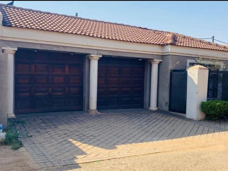 Front elevation of the property featuring a double garage with wooden doors, paved driveway, and decorative columns under a tiled roof.