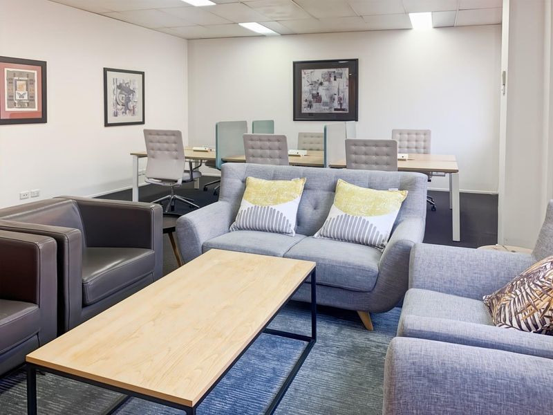 A professional office space featuring a lounge area, carpeted flooring, and a suspended ceiling with recessed lighting.
