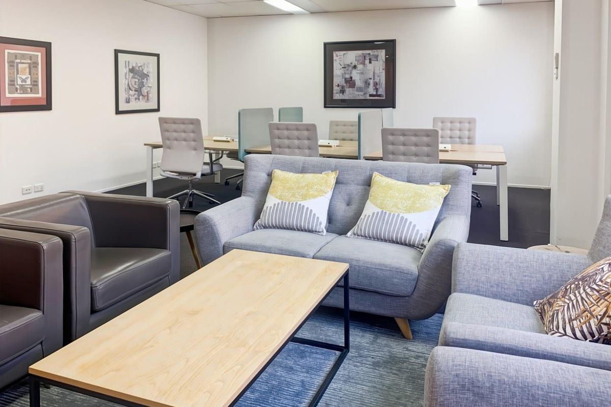 A professional office space featuring a lounge area, carpeted flooring, and a suspended ceiling with recessed lighting.