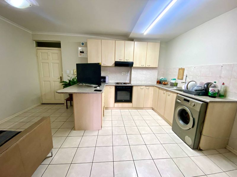Functional kitchen featuring light wood-finish cabinetry, integrated oven and hob, tiled backsplash, and tiled flooring with space for a washing machine.