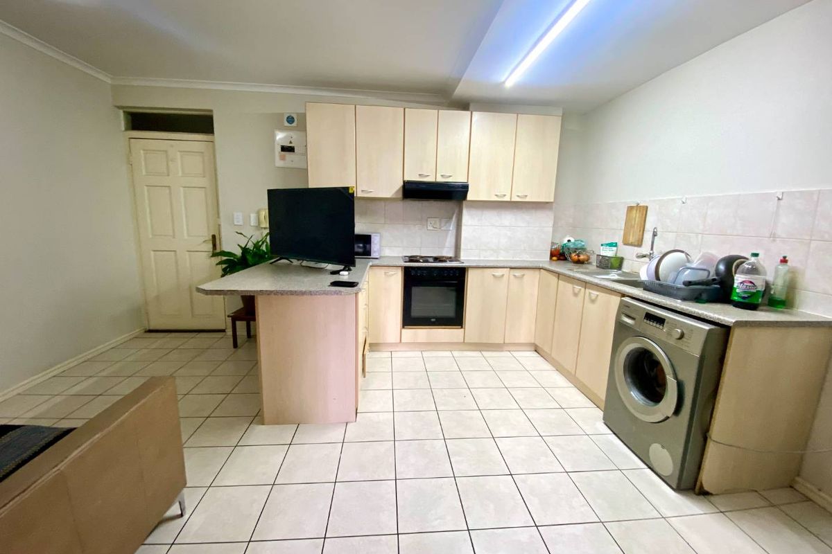 Functional kitchen featuring light wood-finish cabinetry, integrated oven and hob, tiled backsplash, and tiled flooring with space for a washing machine.
