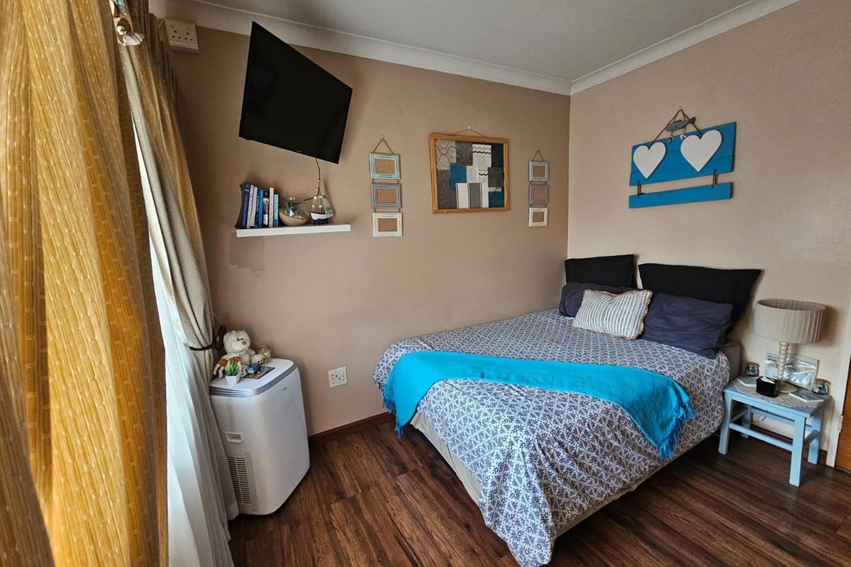 A cozy bedroom featuring wood-look laminate flooring, neutral wall tones, and a wall-mounted television.