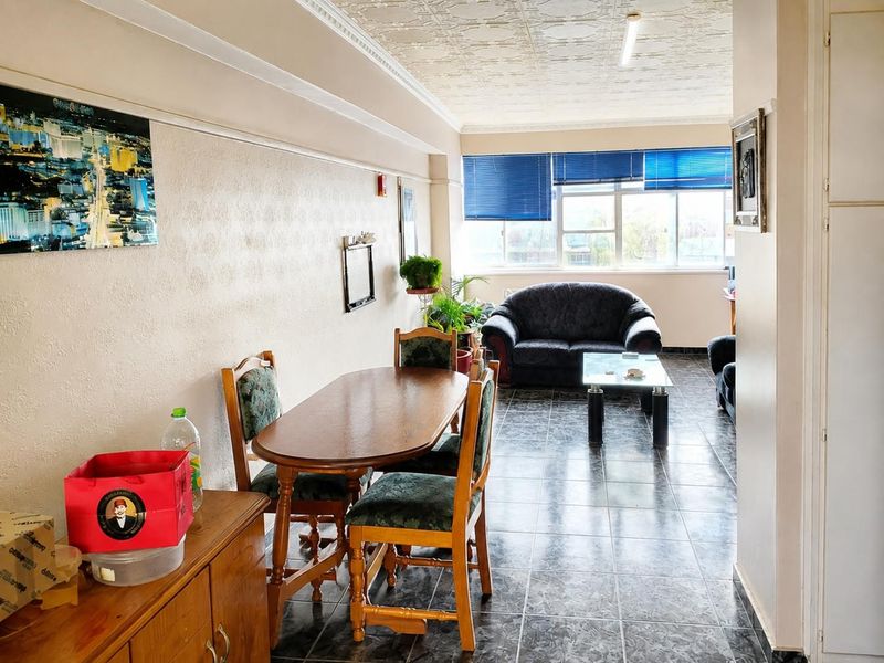 Open-plan living and dining area featuring tiled flooring, decorative ceiling tiles, and large windows with venetian blinds.