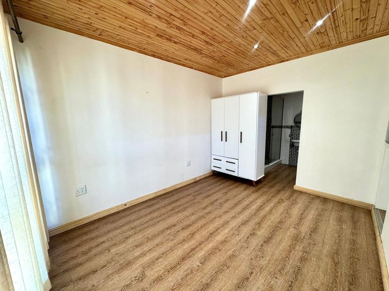 A bedroom featuring timber ceiling paneling and laminate flooring, with an adjoining en-suite bathroom visible through the doorway.
