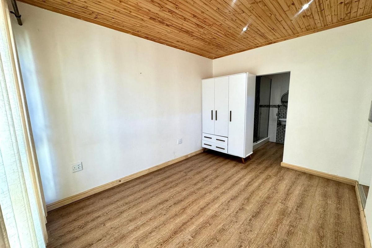 A bedroom featuring timber ceiling paneling and laminate flooring, with an adjoining en-suite bathroom visible through the doorway.