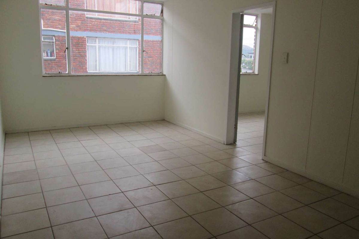 An empty living area featuring large windows, tiled flooring, and a doorway leading to an adjacent room.