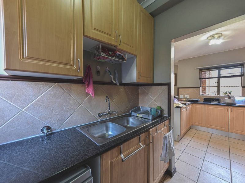 Functional kitchen featuring laminate cabinetry, granite countertops, double stainless steel sink, and tiled flooring, offering a practical layout with ample storage space.