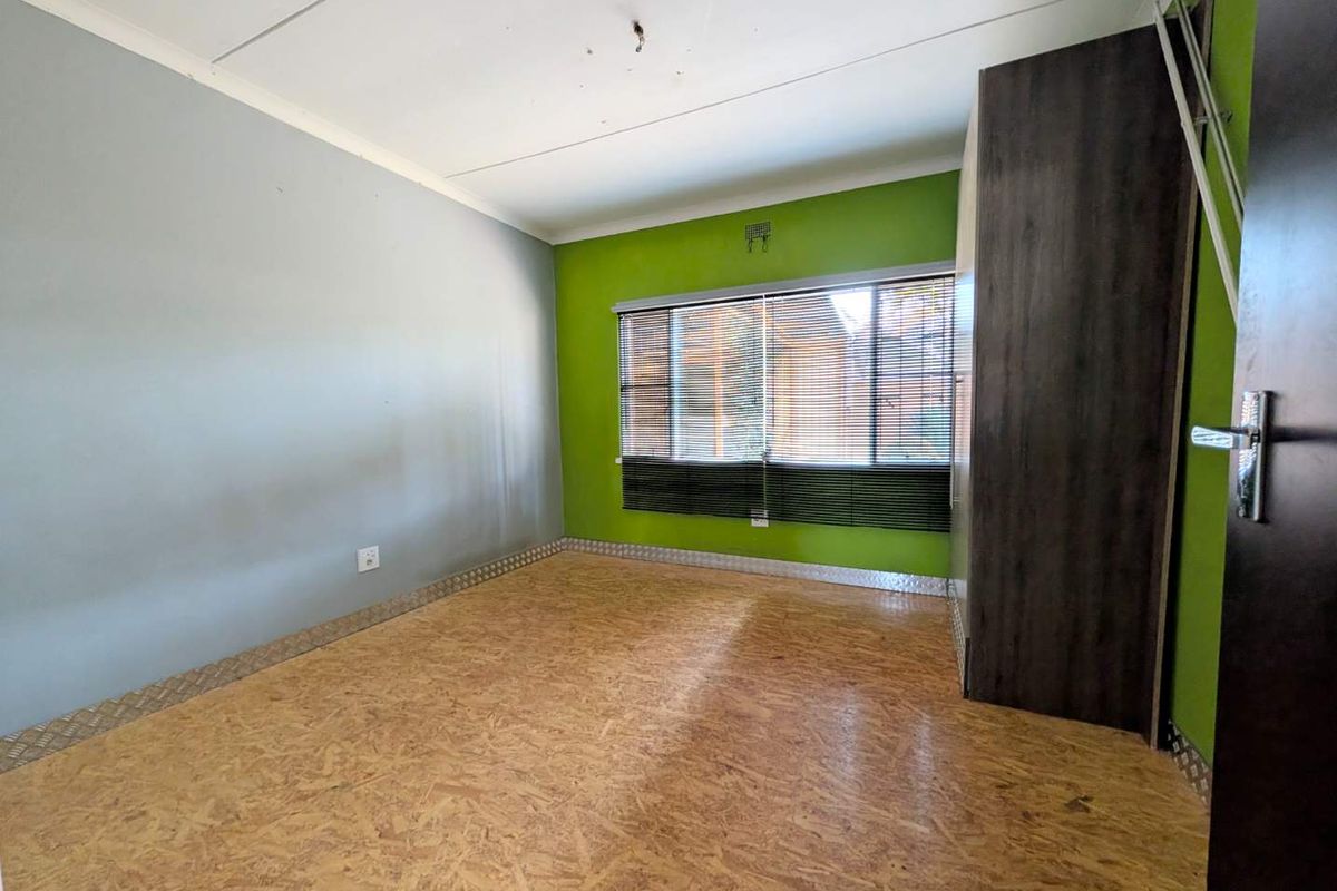 An empty bedroom featuring OSB flooring, built-in wardrobe, and venetian blinds. The room requires minor cosmetic updates and a new light fixture.