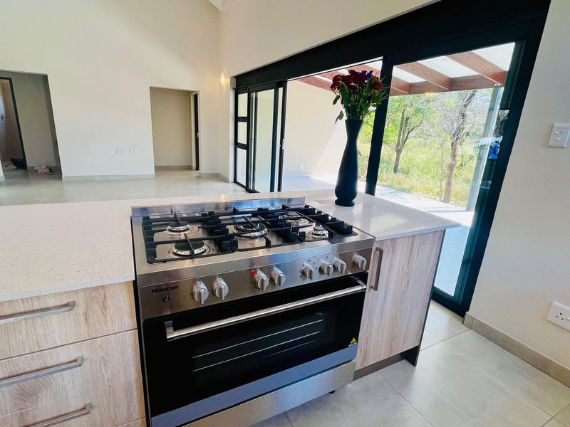 Modern kitchen featuring a gas stove, stone countertops, and light wood cabinetry, with large sliding doors opening to an outdoor patio area.