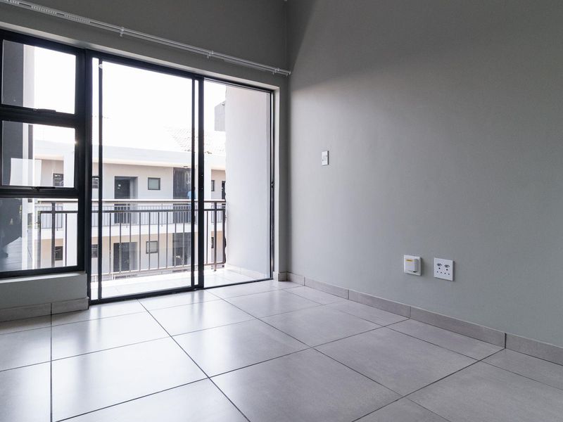 A bright, empty living area featuring modern tiled flooring and a large sliding glass door that opens onto a private balcony.