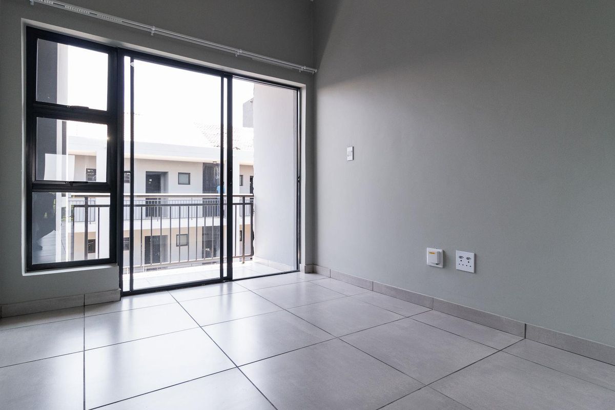 A bright, empty living area featuring modern tiled flooring and a large sliding glass door that opens onto a private balcony.