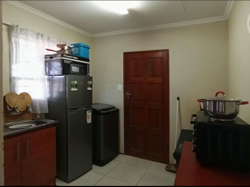 A functional laundry area featuring tiled flooring, built-in cabinetry with a sink, and a solid timber door.