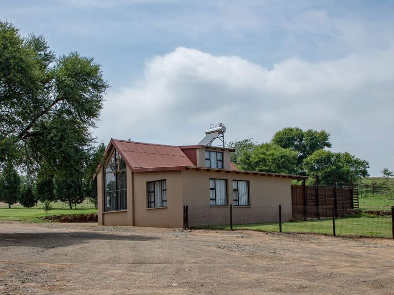 A farm-style dwelling featuring a corrugated metal roof, solar water heating system, and large windows set within a rural landscape.