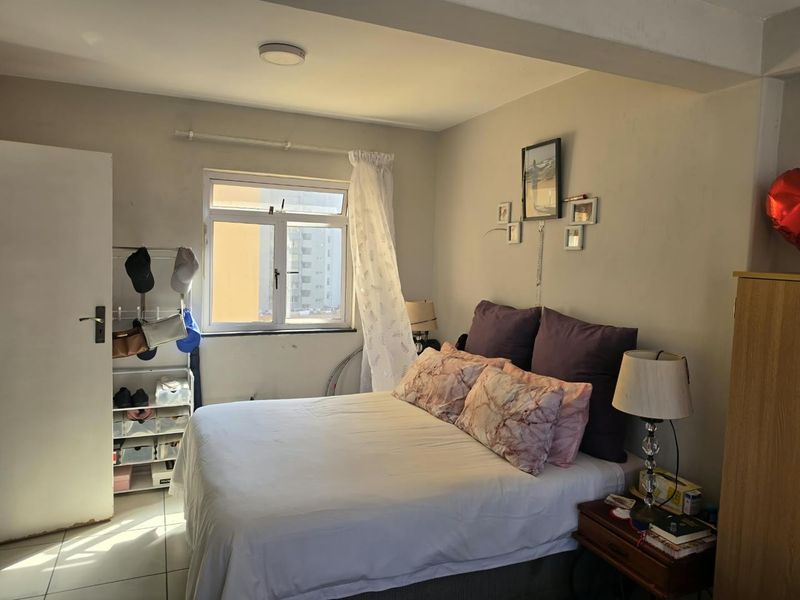 A functional bedroom featuring tiled flooring, a window with natural light, and a standard ceiling light fixture.