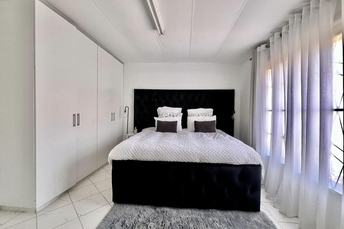A well-maintained bedroom featuring built-in floor-to-ceiling wardrobes, tiled flooring, and large windows allowing for natural light.