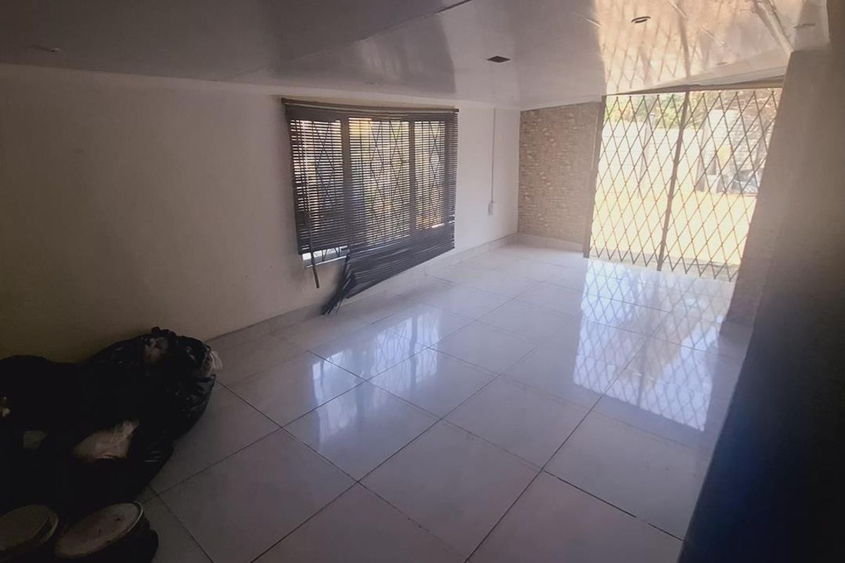 An empty living room featuring large floor tiles, recessed ceiling lights, and a security gate leading to the exterior.