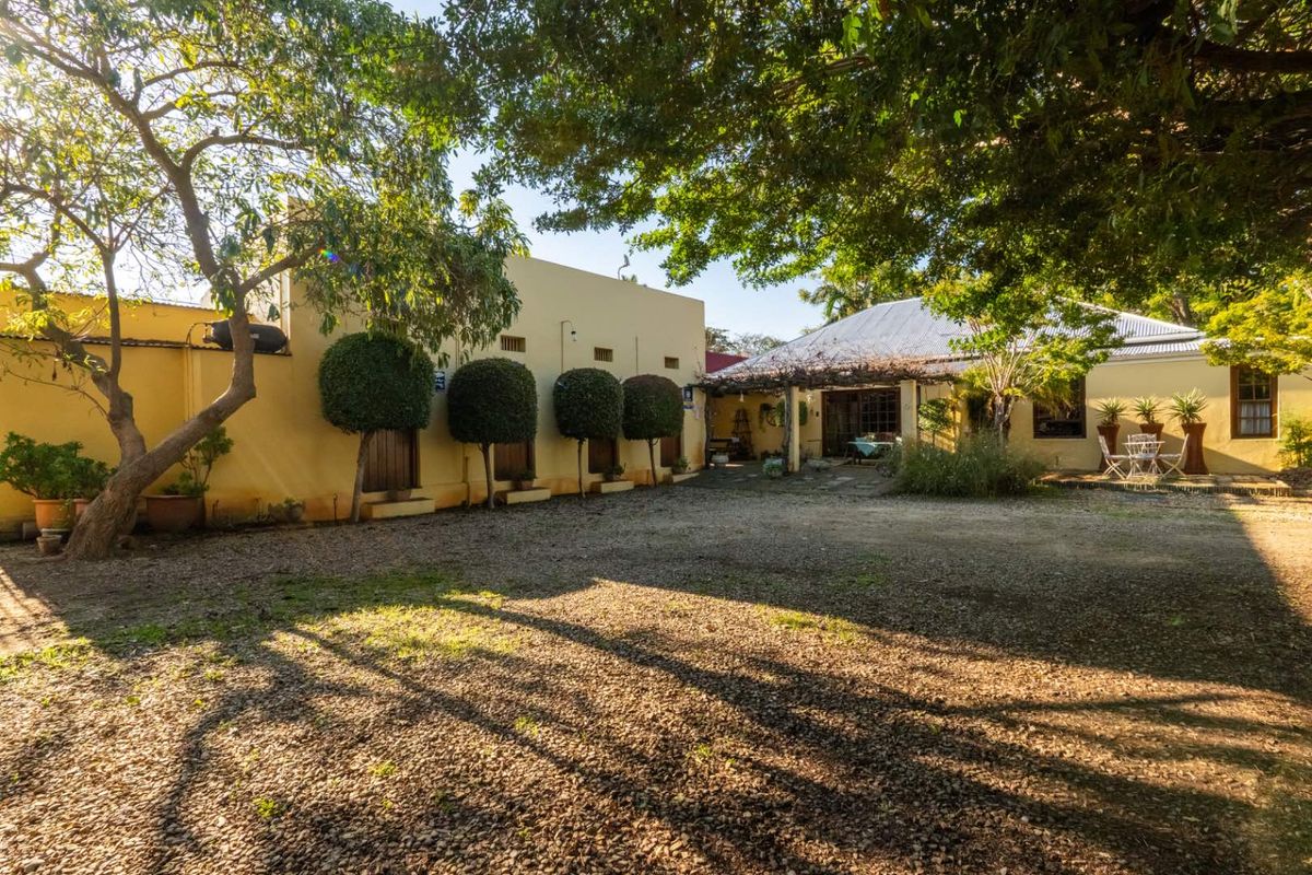 A spacious rear courtyard area featuring a gravel ground surface, mature trees, and access to the main dwelling with a covered patio area.