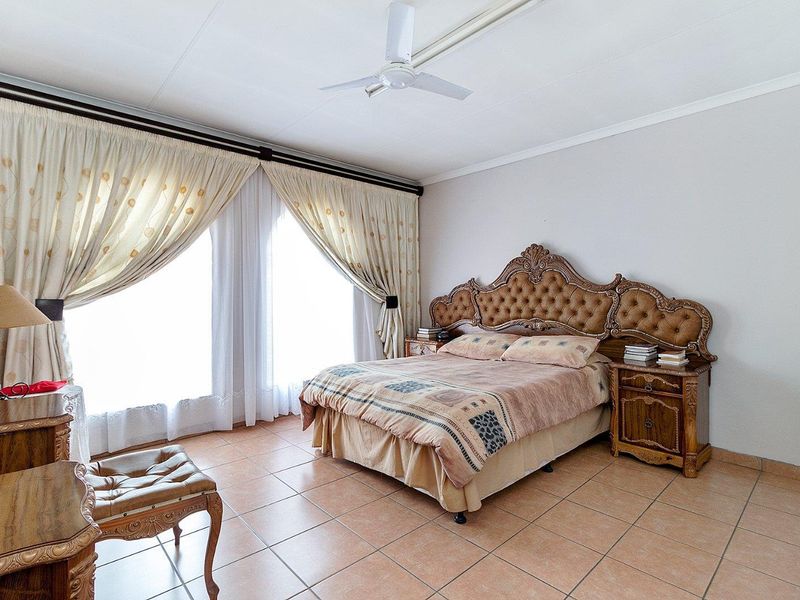 Spacious bedroom featuring neutral tiled flooring, a ceiling fan, and large windows with installed curtain rails, offering a bright and functional living space.