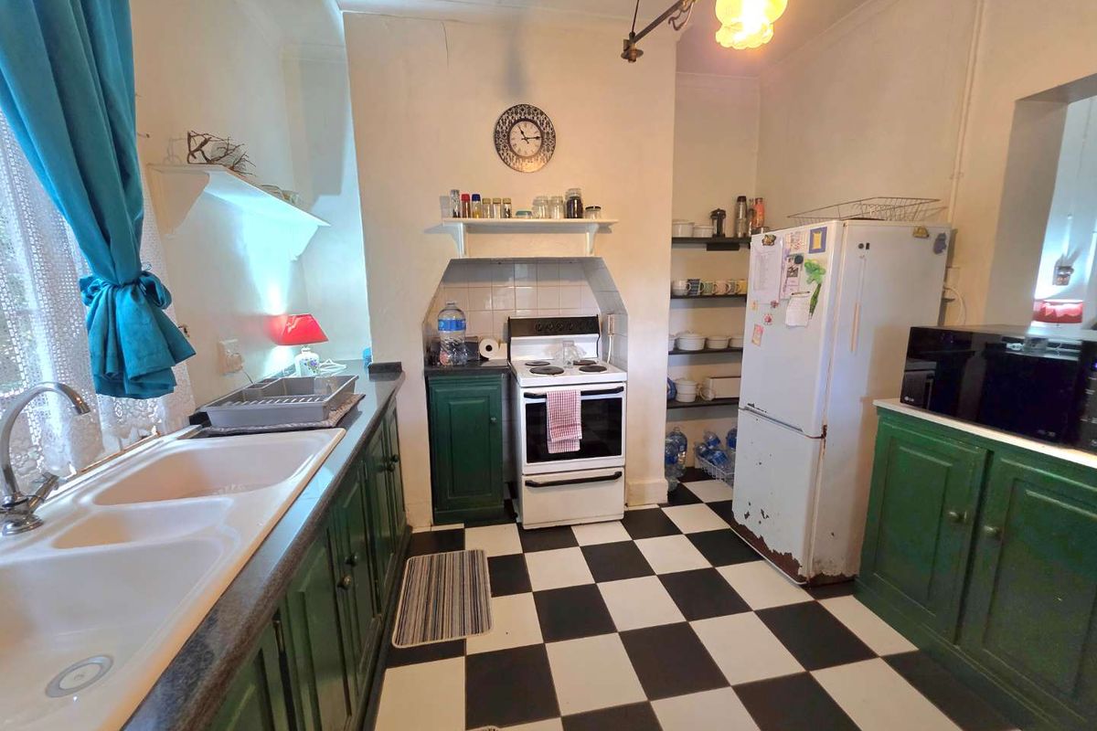 A dated kitchen featuring green cabinetry, a checkerboard floor, and a built-in stove area with open shelving.