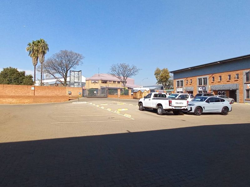 Exterior view of an industrial property complex featuring a paved parking area, brick facade buildings, and secure perimeter walling.