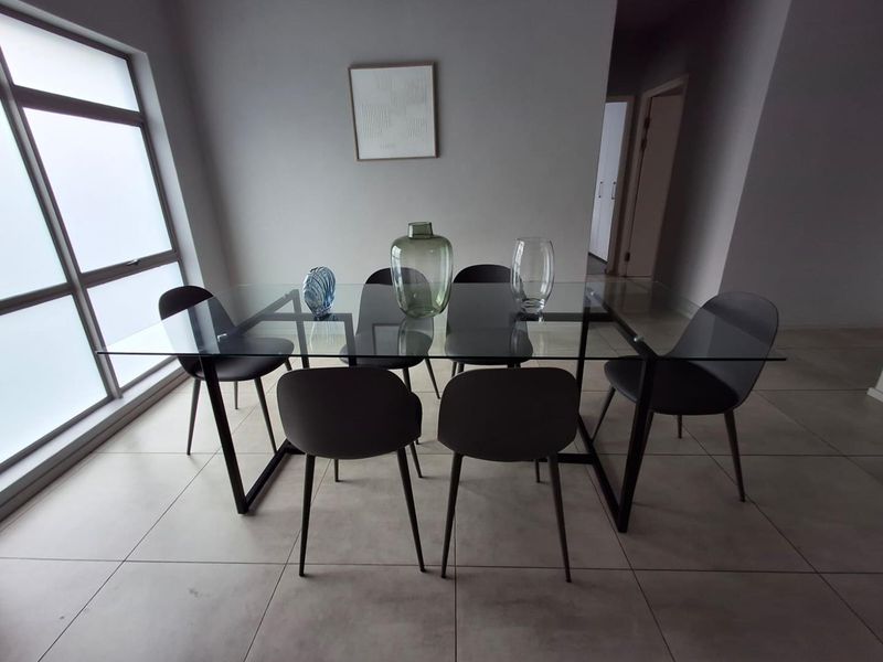 A bright dining area featuring large windows and neutral tiled flooring, providing a clean and modern space for meals.