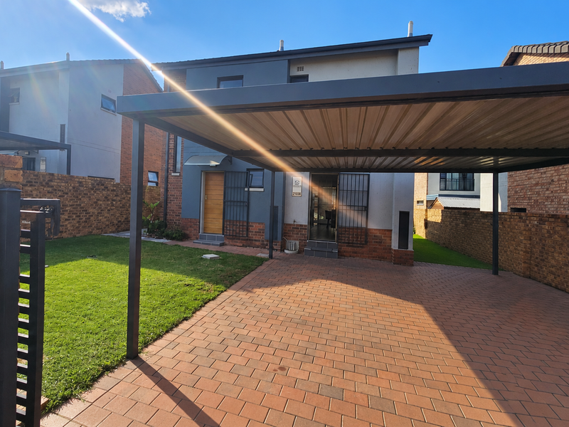 Front exterior view featuring a paved driveway, covered carport, and brick boundary wall with secure gated access to the property entrance.