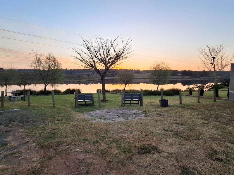 A scenic view of a tranquil lake at sunset, featuring a well-maintained lawn and perimeter fencing on the property grounds.