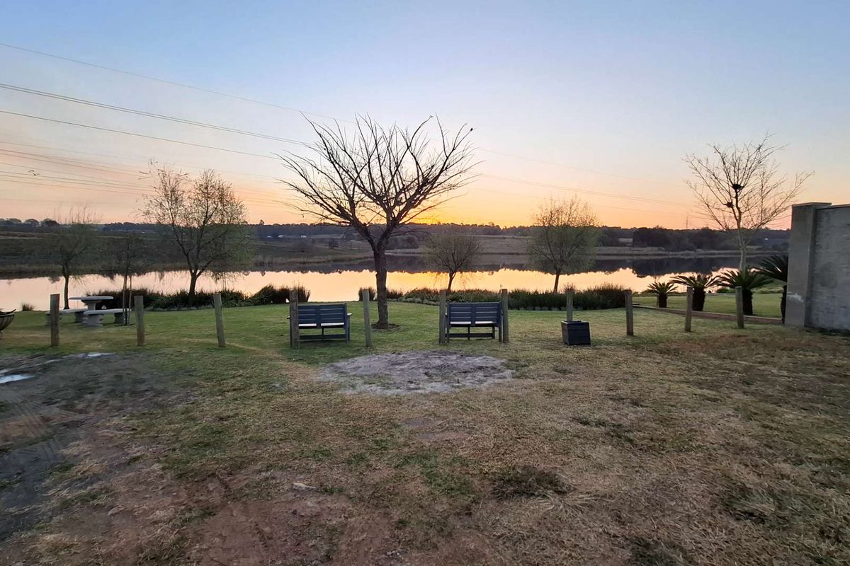 A scenic view of a tranquil lake at sunset, featuring a well-maintained lawn and perimeter fencing on the property grounds.