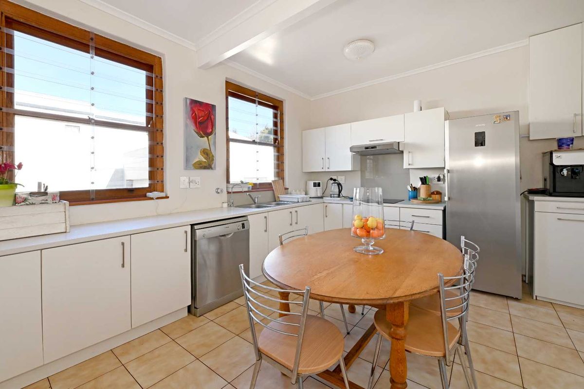 A functional kitchen featuring white cabinetry, tiled flooring, stainless steel sink, and louver windows, providing a bright and practical workspace.
