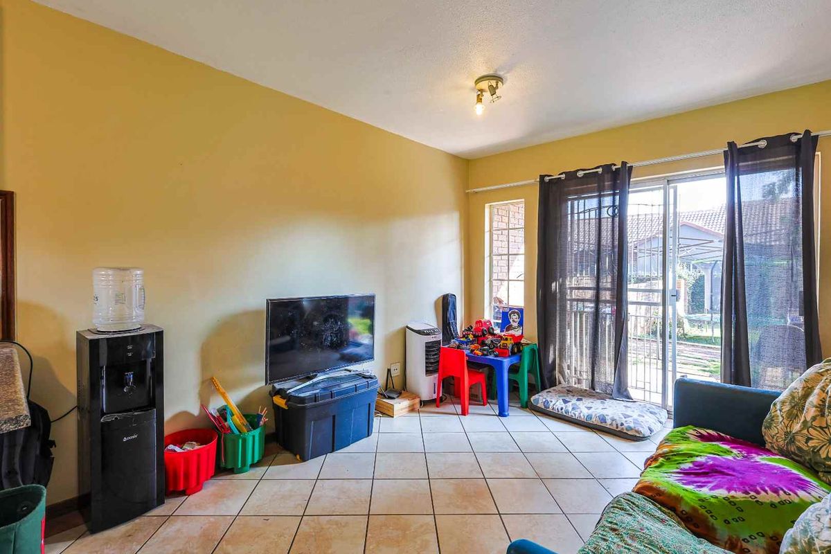 A living room featuring tiled flooring and a sliding glass door with security gate providing access to the exterior.