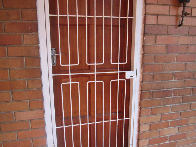 A secure entrance featuring a timber door protected by a white metal security gate set within a face brick wall.