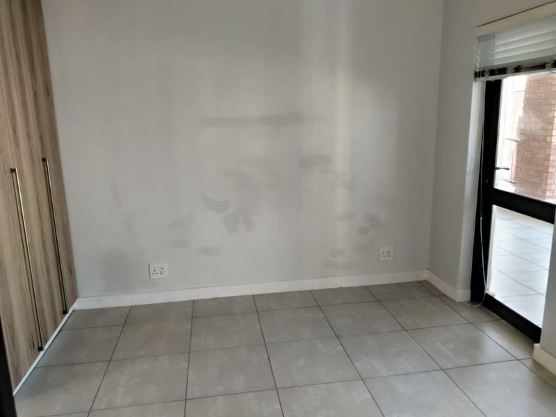 A vacant bedroom featuring tiled flooring, built-in cupboards, and a glass door leading to an outdoor area. The walls require repainting.
