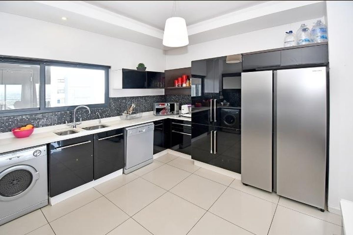 Modern kitchen featuring high-gloss black cabinetry, stone countertops, mosaic tile backsplash, and integrated stainless steel appliances.