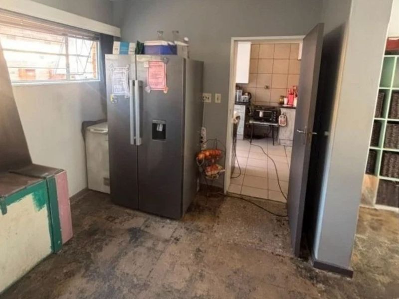 A utility or scullery area showing significant wear on the flooring and walls, with a doorway leading into an adjacent kitchen space.
