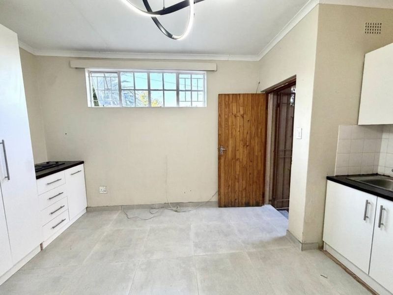 A functional kitchen area featuring white built-in cabinetry, dark countertops, tiled flooring, and a built-in hob, offering a clean and practical workspace.