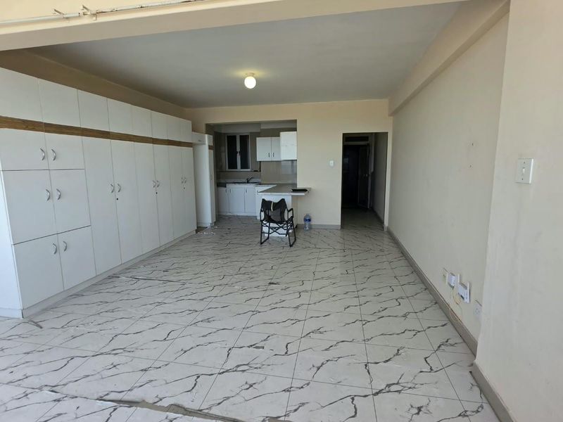 Open plan living area featuring extensive built-in storage cupboards and a compact kitchen space with tiled flooring throughout.