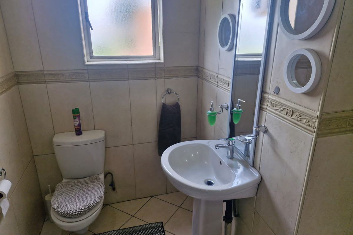 A compact bathroom featuring a pedestal sink, a standard toilet, and full-height wall tiling with a decorative border.