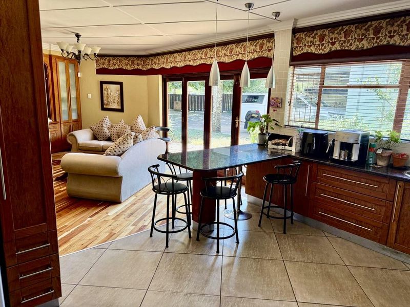 Open-plan kitchen and living area featuring a breakfast bar, granite countertops, wooden cabinetry, and seamless transition to the outdoor space via folding glass doors.