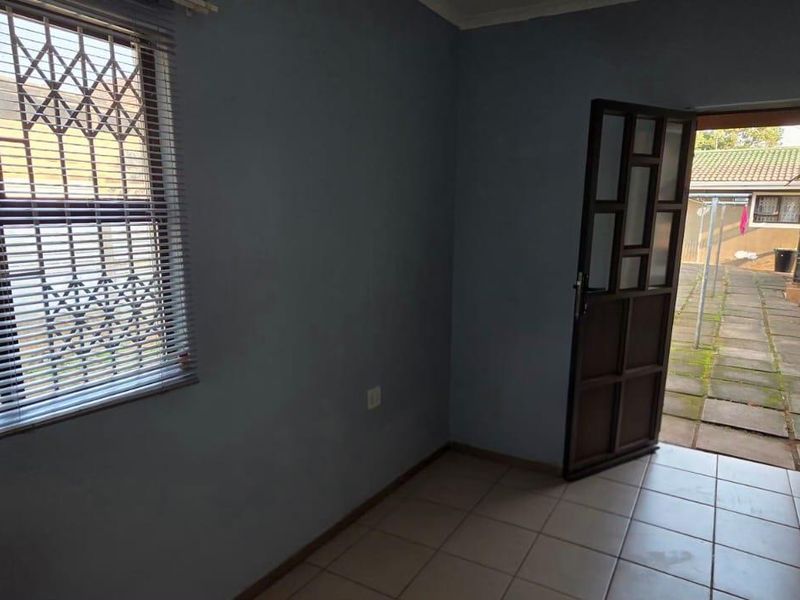 An empty living area featuring tiled flooring, a window with security bars, and direct access to an outdoor paved area.