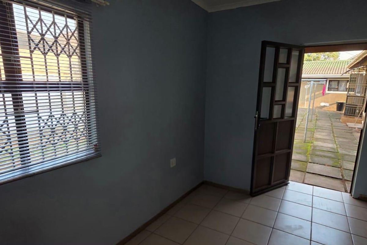 An empty living area featuring tiled flooring, a window with security bars, and direct access to an outdoor paved area.