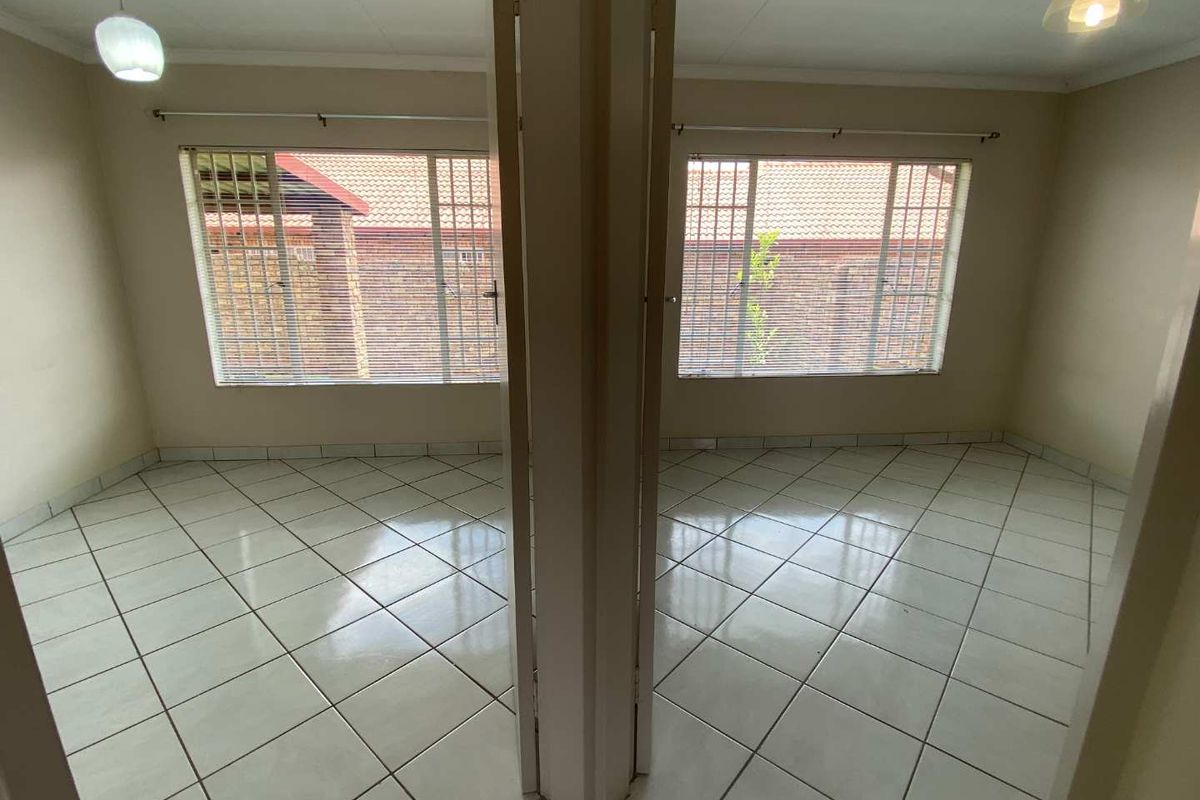 A bright, empty bedroom featuring tiled flooring, large windows with security bars, and neutral wall finishes, offering a clean canvas for personalization.