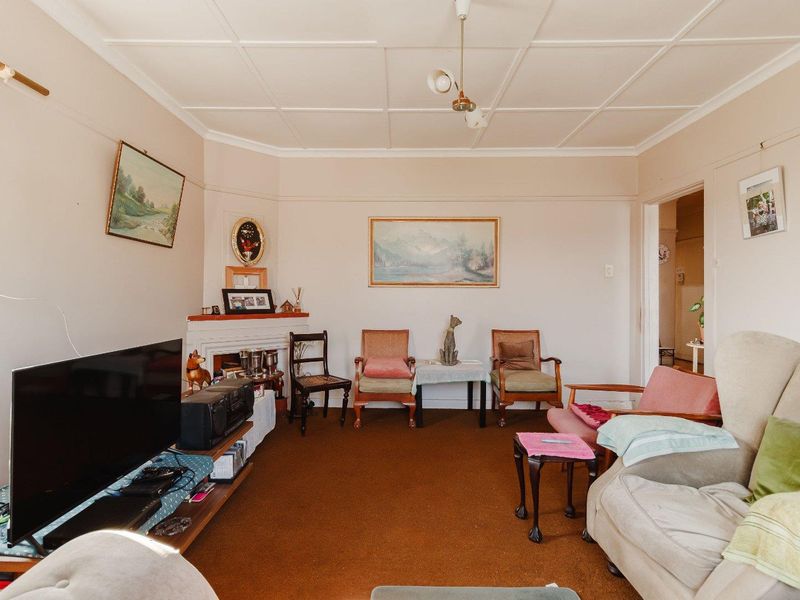 A traditional living room featuring a fireplace with a mantelpiece, classic ceiling tiles, and carpet flooring, offering a dated but functional space.