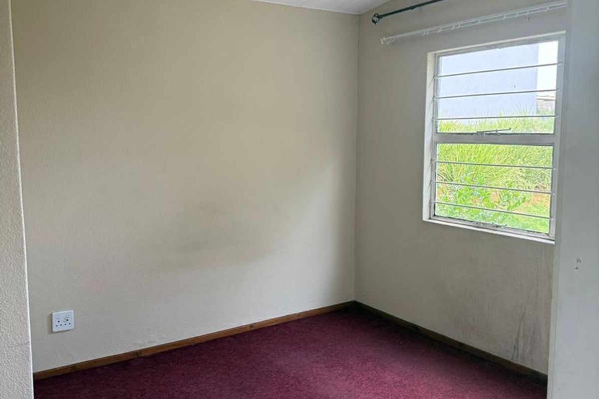 A vacant bedroom featuring a window with security bars, carpeted flooring, and neutral wall finishes, ready for renovation or personalization.